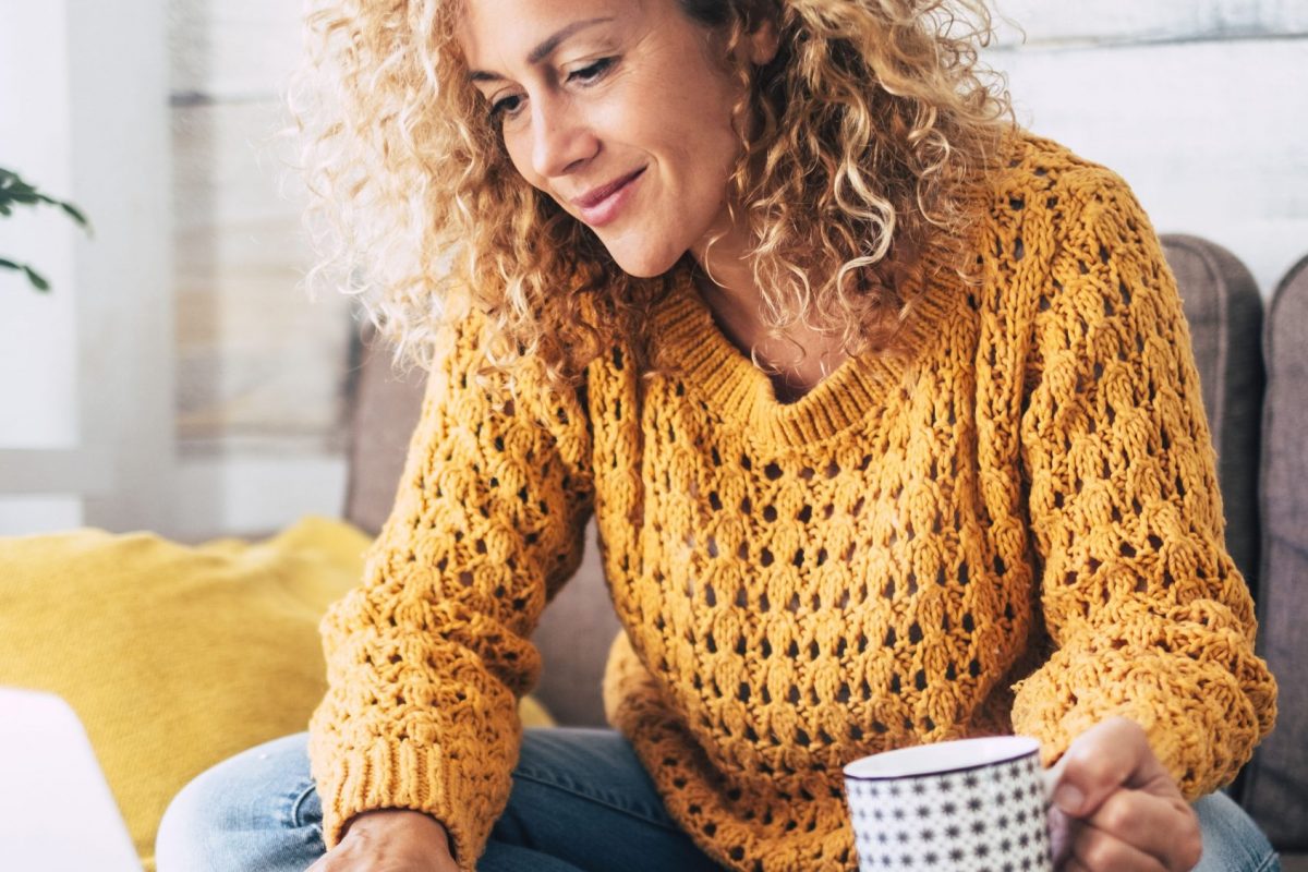 Nice beautiful lady with blonde curly hair work at the notebook sit down on the sofa at home - check on line shops for cyber monday sales - technology woman concept for alternative office freelance