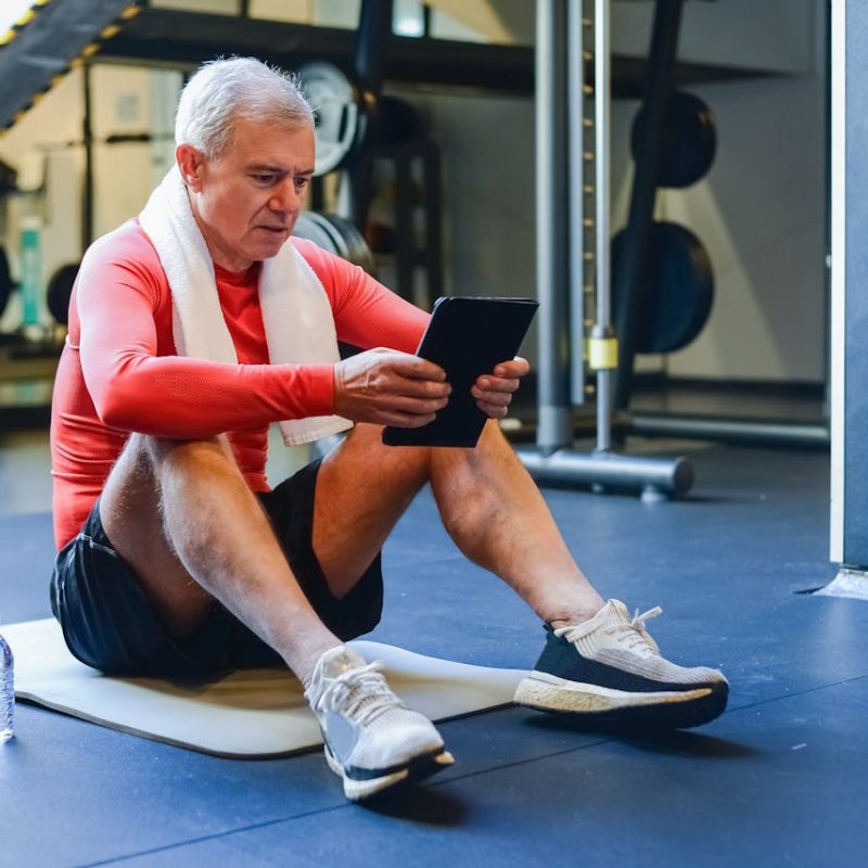 Senior Living Wellness with Digital Tools and Health Coaching Older adult man using a digital wellness platform on a tablet in a gym, representing health coaching and fitness tools for senior living communities.