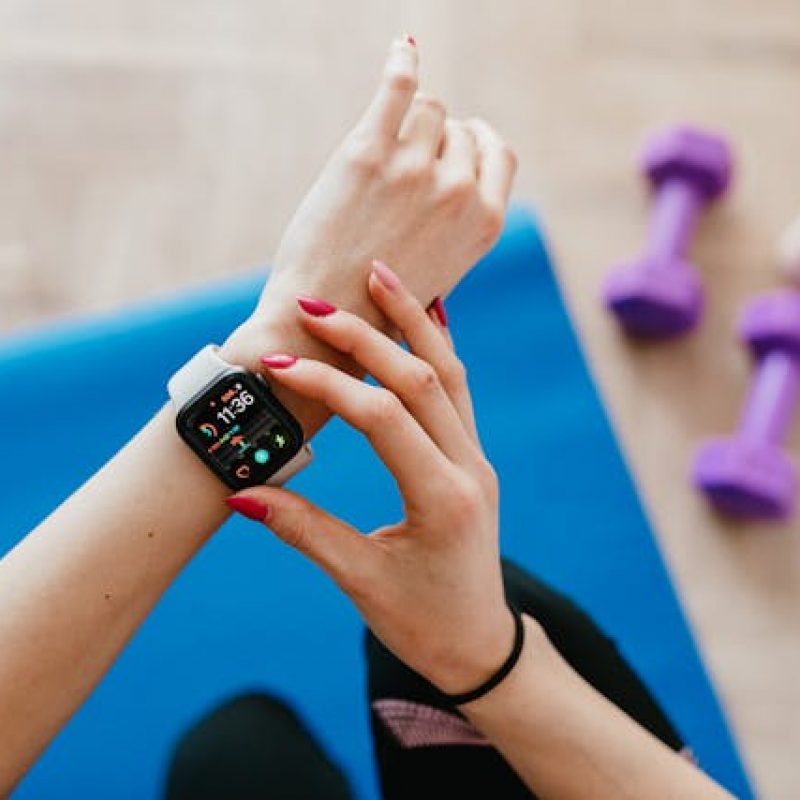 Smart Recovery with Your Wearable – Avidon Health Woman checking smartwatch on yoga mat with light weights nearby, illustrating smart recovery using wearable technology.