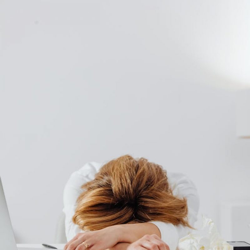 A woman slumped over her desk with her head on her arms, representing remote work fatigue and the importance of workplace wellness through movement.