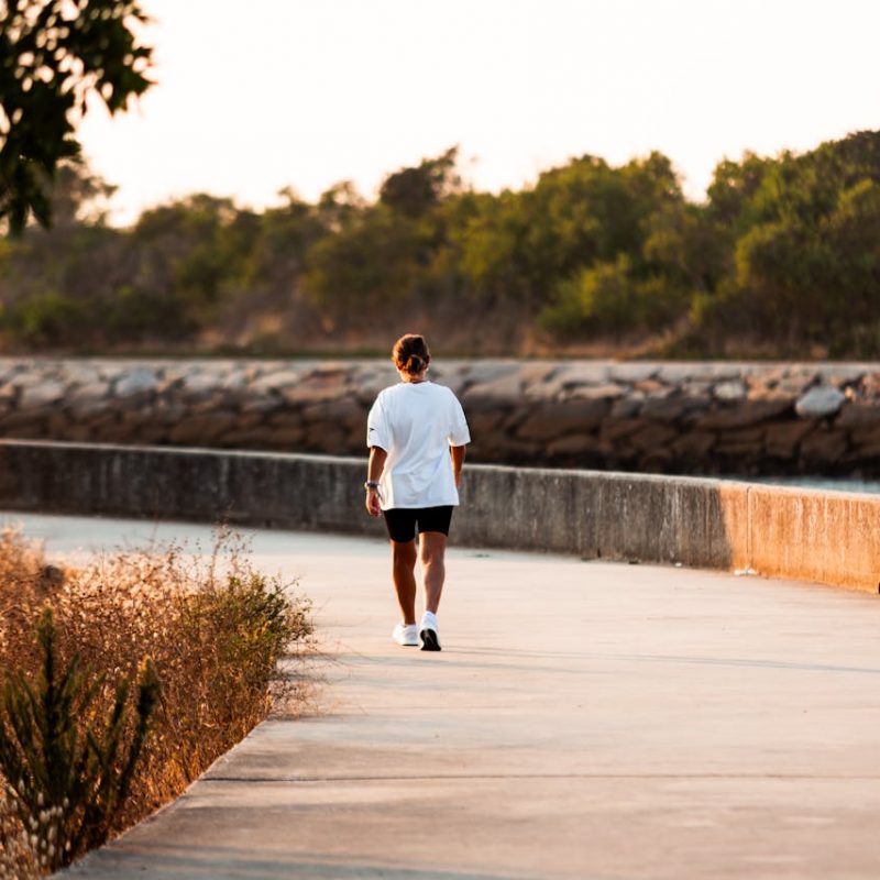 A Health Coach’s Journey: Meeting People Where They Are Walking a sunlit path by the water—symbolizing a health coach journey built on small, steady steps