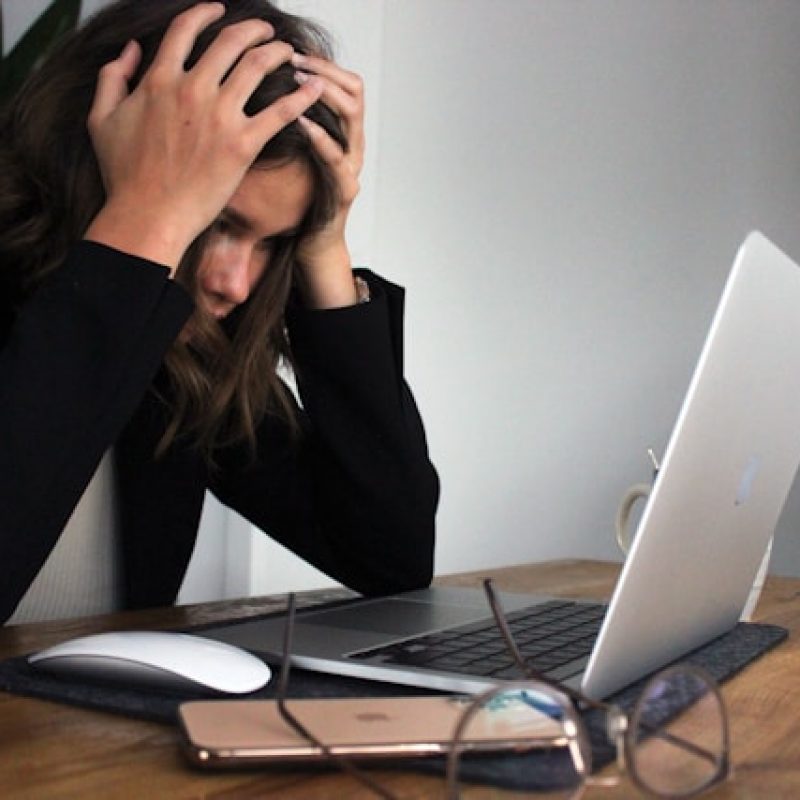 Woman sitting at a laptop with her head in her hands, appearing stressed and overwhelmed — illustrating the need for quick micro-resets and 2-minute stress breaks.