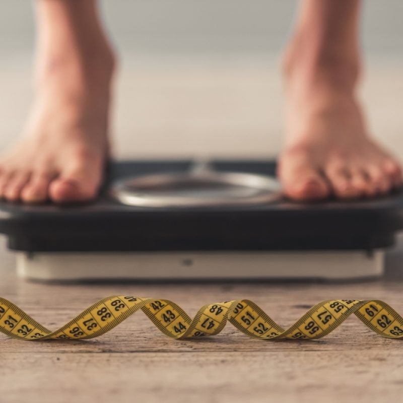 Feet on a bathroom scale with a measuring tape, representing habits and body confidence.